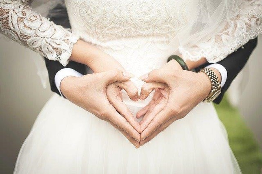 Husband and wife holding hands in the shape of a heart on their wedding day. This lovely photo shows the critical need for Wedding Planner Insurance.